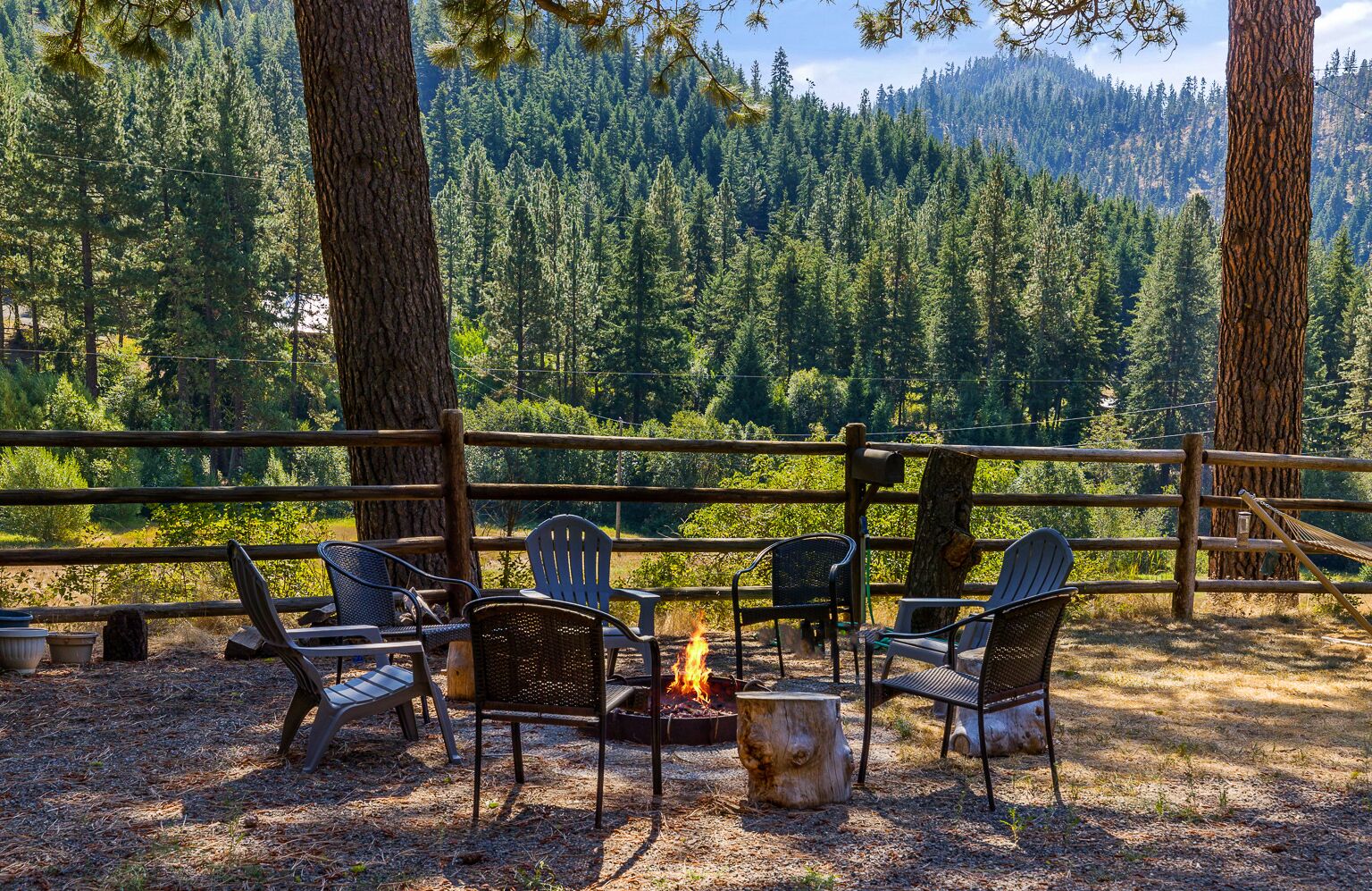 An outdoor seating area with chairs and a fire pit, surrounded by a wooden fence and tall trees.