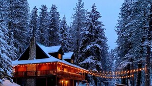 A snow-covered lodge with a stone chimney, wooden exterior, and string lights. - Private Cabin on 3 Acres for Outdoor Enthusiasts  (Cle Elum)