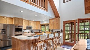 A spacious kitchen with wooden cabinets, a large island with bar stools, stainless steel appliances, and a view through a glass door to the outdoors. - Private Cabin on 3 Acres for Outdoor Enthusiasts  (Cle Elum)