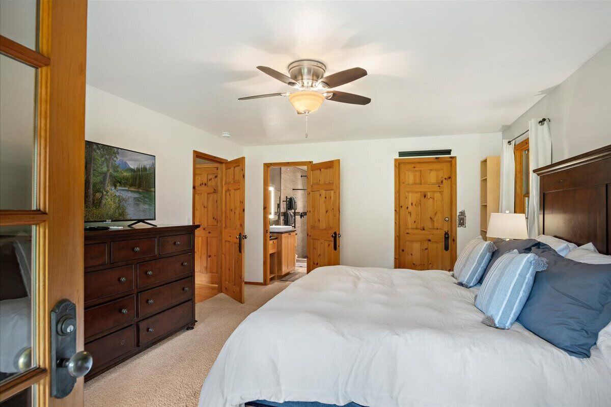 A bedroom with a large bed, wooden wardrobe, ceiling fan, and a television on a dresser.