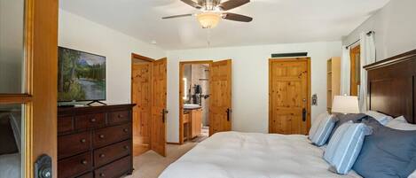 A bedroom with a large bed, wooden wardrobe, ceiling fan, and a television on a dresser.