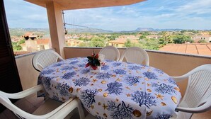 A balcony with a table and chairs, a view of a town, and a mountain in the distance.
