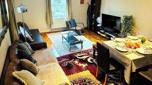 A living room with a sofa, a dining table set for two, a television, and a bookshelf.