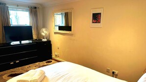 A hotel room with a bed, a TV, a dresser, a mirror, and a window with curtains.