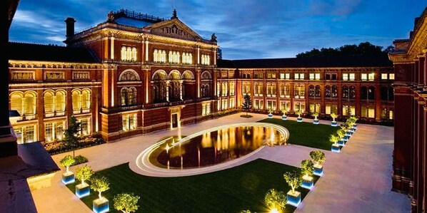 Un gran edificio iluminado, con un patio central y una piscina reflectante.