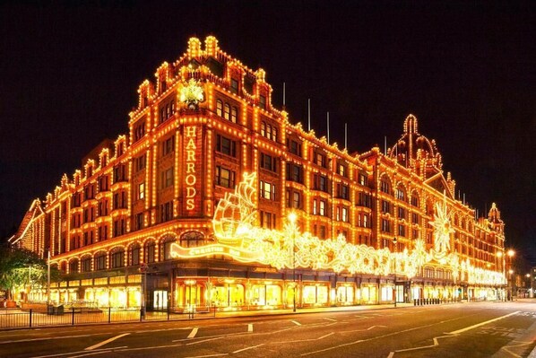 Un edificio grande y ornamentado con el nombre "HARRODS" en relieve, que presenta detalles arquitectónicos clásicos e iluminación extensa.