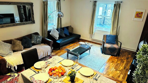 A dining area with a table set for four, a sofa, a chair, and a potted plant.