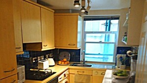 A compact kitchen with wooden cabinets, a stove, an oven, a washing machine, a sink, and a window.