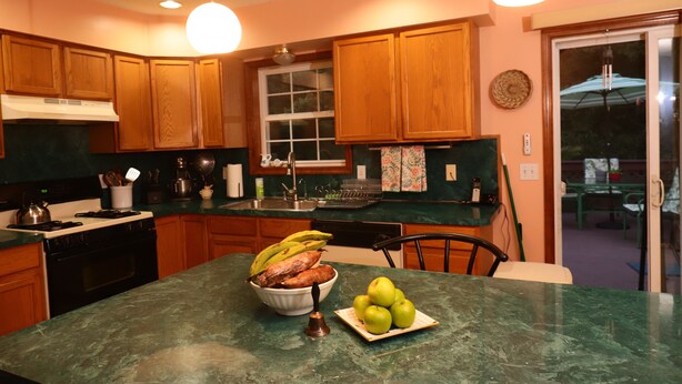 A kitchen with wooden cabinets, a stove, and a bowl of fruit on the counter.