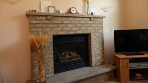 A brick fireplace with a mantel, a TV on a wooden stand, and a vase of dried plants.