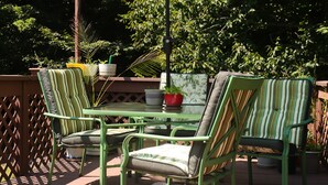 A patio with green metal chairs and a table, surrounded by potted plants and a striped umbrella.