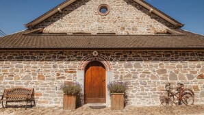 A stone building with a wooden door, a bench, and a bicycle. - La Bushaye - Cottage L'Etable (Aubel)