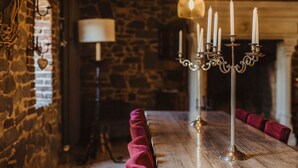 A long wooden table with a velvet cushion, a candelabra with candles, and a stone wall with a fireplace in the background. - La Bushaye - Cottage L'Etable (Aubel)