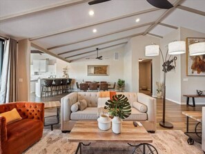Relax in this inviting living room with a sofa, armchair, and coffee table, surrounded by a large potted plant.