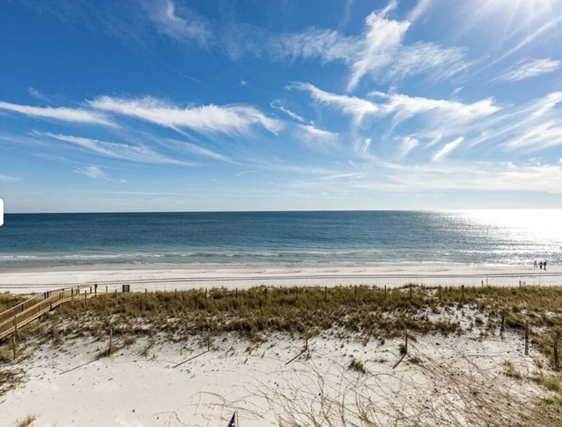 A beach with a wooden walkway leading to the shore, sandy dunes, and a clear blue sky.
