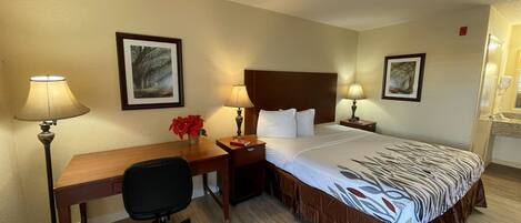 A hotel room with a bed, desk, chair, lamps, and framed pictures on the walls.