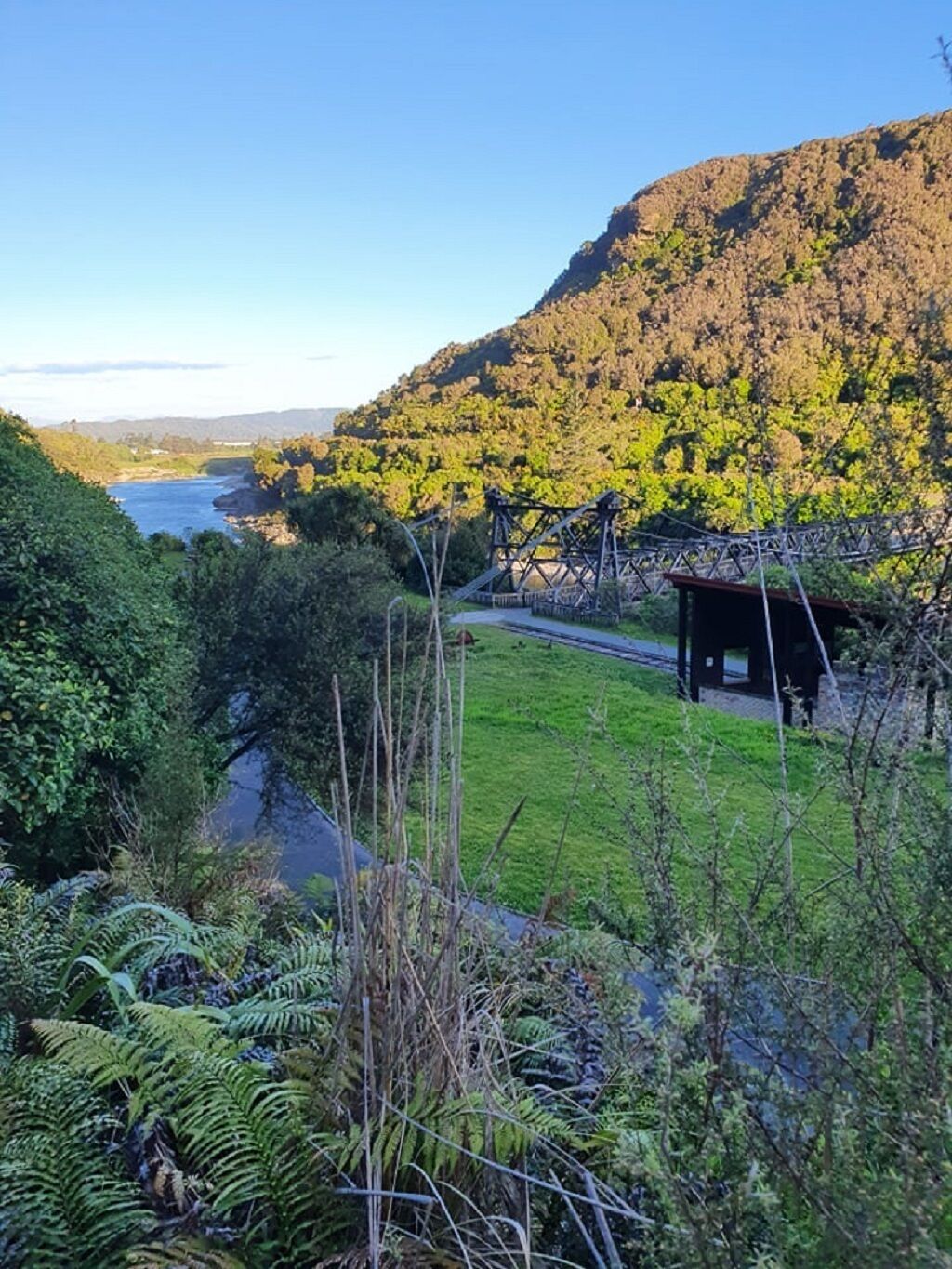 Vista al río con una estructura de madera, abundante vegetación y montañas al fondo.
