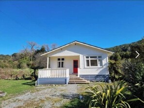 Situated in a lush landscape, this charming house features a front porch and a grassy lawn.