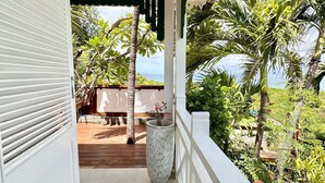 A covered balcony with a view of the ocean, surrounded by tropical plants and a wooden deck. - Rêves de Soleil: Sweet Sunset Lodge with panoramic sea view (Sainte-Anne)