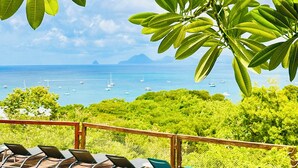 A poolside area with lounge chairs and a view of the ocean. - Rêves de Soleil: Sweet Sunset Lodge with panoramic sea view (Sainte-Anne)
