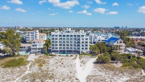 Un hotel de varios pisos con piscina, rodeado por una playa y otros edificios.