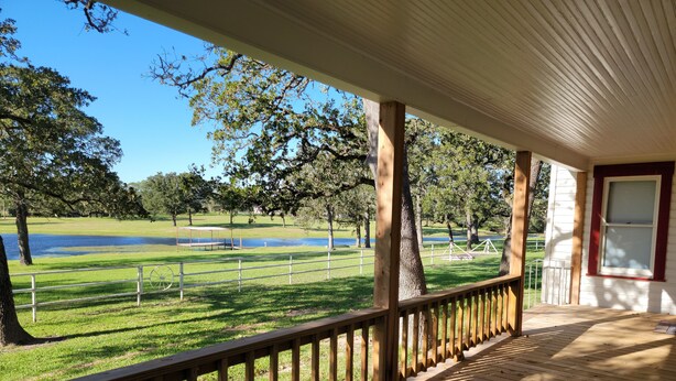 A wooden deck with a railing overlooking a grassy area with a pond and trees. - Country house minutes from Aggieland  (College Station)