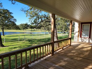 Une terrasse en bois, dotée d’une rambarde, qui donne sur une zone verdoyante avec un étang et des arbres.