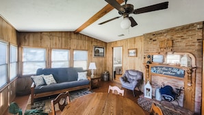 A cozy room with wooden walls, a blue sofa, a wooden table, and a fireplace with a sign. - Country house minutes from Aggieland  (College Station)