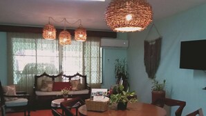 Un área de comedor con una mesa redonda de madera, cuatro sillas, un sofá con cojines e iluminación colgante de fibras trenzadas.