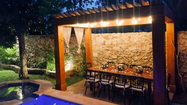 Un patio exterior con un muro de piedra, una pérgola de madera y una piscina.