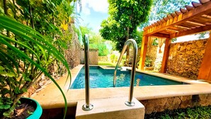 Una piscina con escalones de acceso, rodeada de vegetación y muros de piedra.