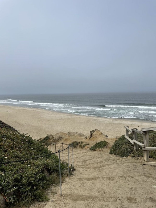 A sandy beach with a wooden staircase leading down to the shore, overlooking the ocean.