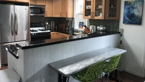 Una cuina moderna amb armaris de fusta, electrodomèstics d'acer inoxidable, taulell negre i una cadira verda.