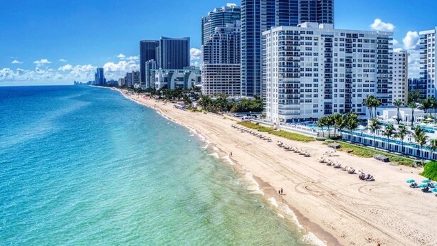A beach with high-rise buildings, clear blue water, and a sandy shore.