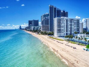 A beach with high-rise buildings, clear blue water, and a sandy shore.