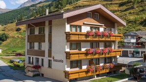 Ein mehrstöckiges Hotel mit Balkonen, die mit Blumen geschmückt sind, vor einer Berglandschaft.