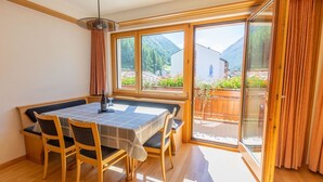 Ein Essbereich mit Tisch und Stühlen, großen Fenstern und Blick auf eine Berglandschaft.