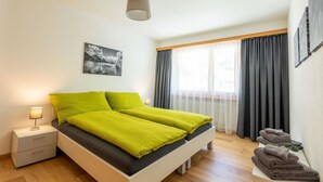 Ein modernes Schlafzimmer mit Bett, Nachttisch, Lampe, einem Bild an der Wand und einem Fenster mit Vorhängen.
