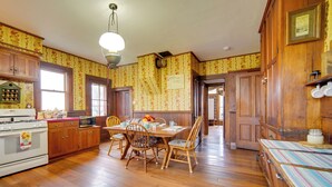 A traditional kitchen with wooden cabinets, a dining table with chairs, and a vintage stove. - Historic Victorian Farmhouse w/ Porch & Views! (Mayville)