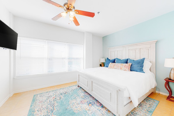 A bedroom with a white bed, a ceiling fan, a window with blinds, and a patterned rug. - Lovely Townhome w/Shared Pool, Central AC, WiFi - Short Walk to Beach (South Padre Island)