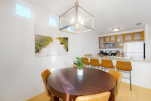 A modern kitchen with a central island, wooden cabinets, and a dining area with a round table and chairs. - Lovely Townhome w/Shared Pool, Central AC, WiFi - Short Walk to Beach (South Padre Island)