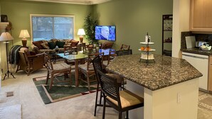 Una cocina moderna y zona de estar con mesa, sillas, televisor y una pequeña isla con fregadero.