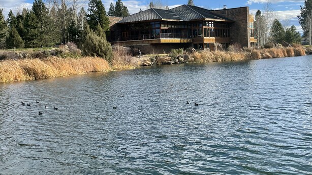 Una cabaña junto a un lago con un edificio grande que tiene varias ventanas y un balcón.