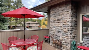 Un patio con un muro de piedra, una sombrilla roja y una mesa de metal con sillas.