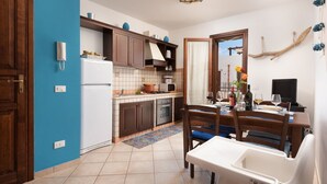 A compact kitchen with a refrigerator, stove, and wooden cabinets. A dining table with chairs is positioned near a window.