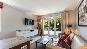 A modern living room with a flat-screen TV, a wooden coffee table, a sofa with cushions, a white console, and a sliding glass door leading to an outdoor area. - The Villa 1903, Whg. 4 - The Villa 1903 (Sylt)
