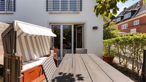 A patio with a wooden table, a cushioned chair, and a sun umbrella. - The Villa 1903, Whg. 4 - The Villa 1903 (Sylt)