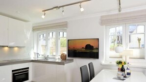 Une cuisine moderne avec des meubles blancs, un four encastré et un coin repas comprenant une table blanche et des chaises noires.