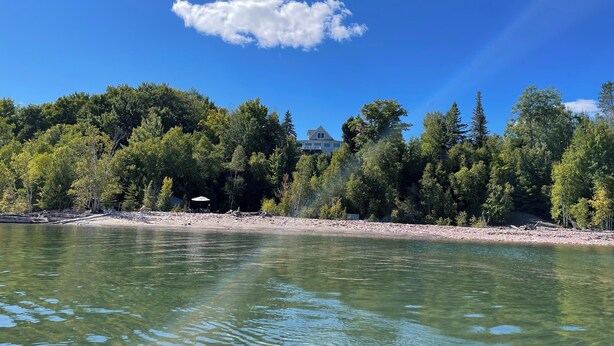 Une vue sur le lac, avec une maison entourée d’arbres denses et un ciel dégagé.