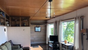 Un salon chaleureux avec un plafond en bois, un téléviseur, un canapé et une fenêtre avec des rideaux.